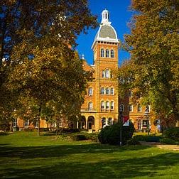A photo of Old Main in Fall, surrounded by trees with green and gold leaves.